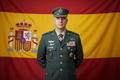 Homem vestido de roupa militar com 35 anos e fundo com bandeira da espanha